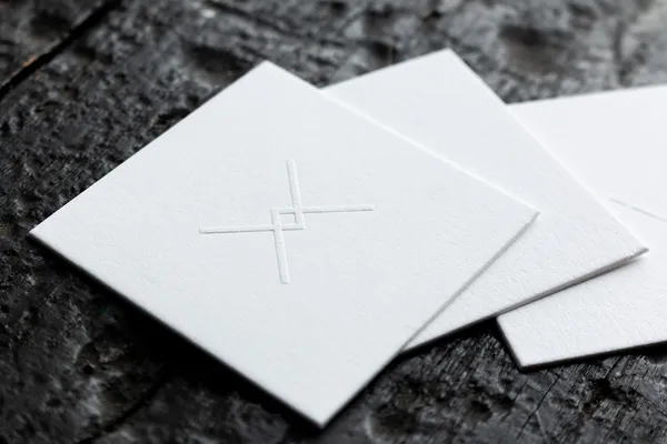 White business cards with blind embossed crosshair logo on thick cotton paper, fanned out on a dark surface