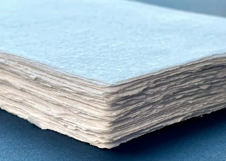 A spread of handmade papers in soft natural tones, showing varied deckled edges and visible fiber texture.