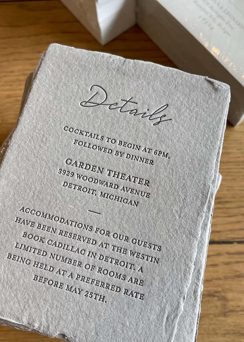 A letterpress-printed wedding invitation on soft gray handmade paper with a deckled edge.