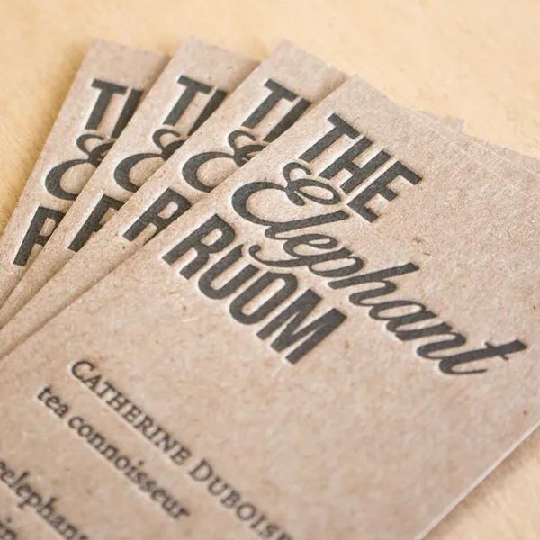 Chipboard business cards fanned on a wood surface, letterpress printed in black ink on recycled board