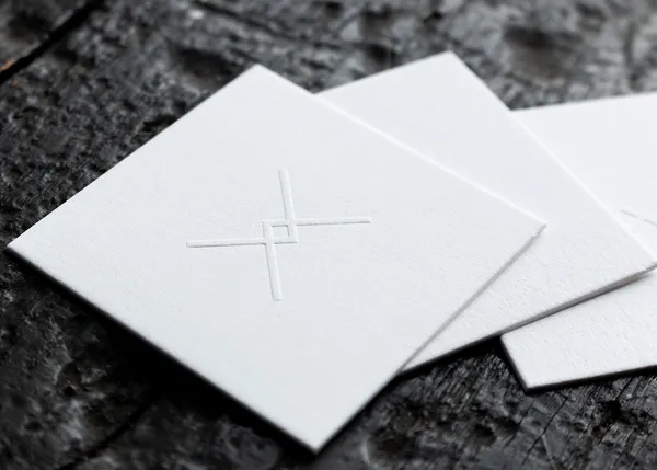 Square business cards in white cotton paper with raised blind embossed crosshair logo